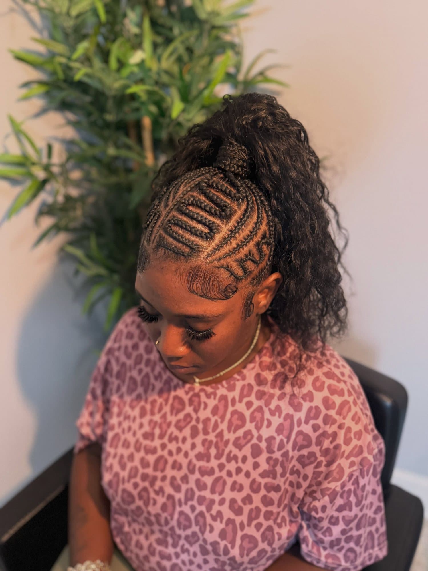 Stitch-braided crown feeding into a high curly ponytail, with looping geometric partings through the sides